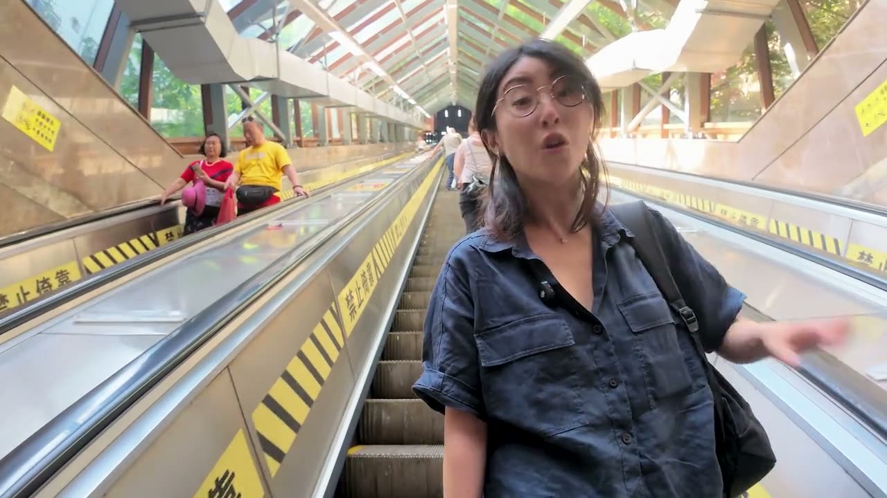 Dami riding the long Huangguan escalator, the ramp stretching away below.